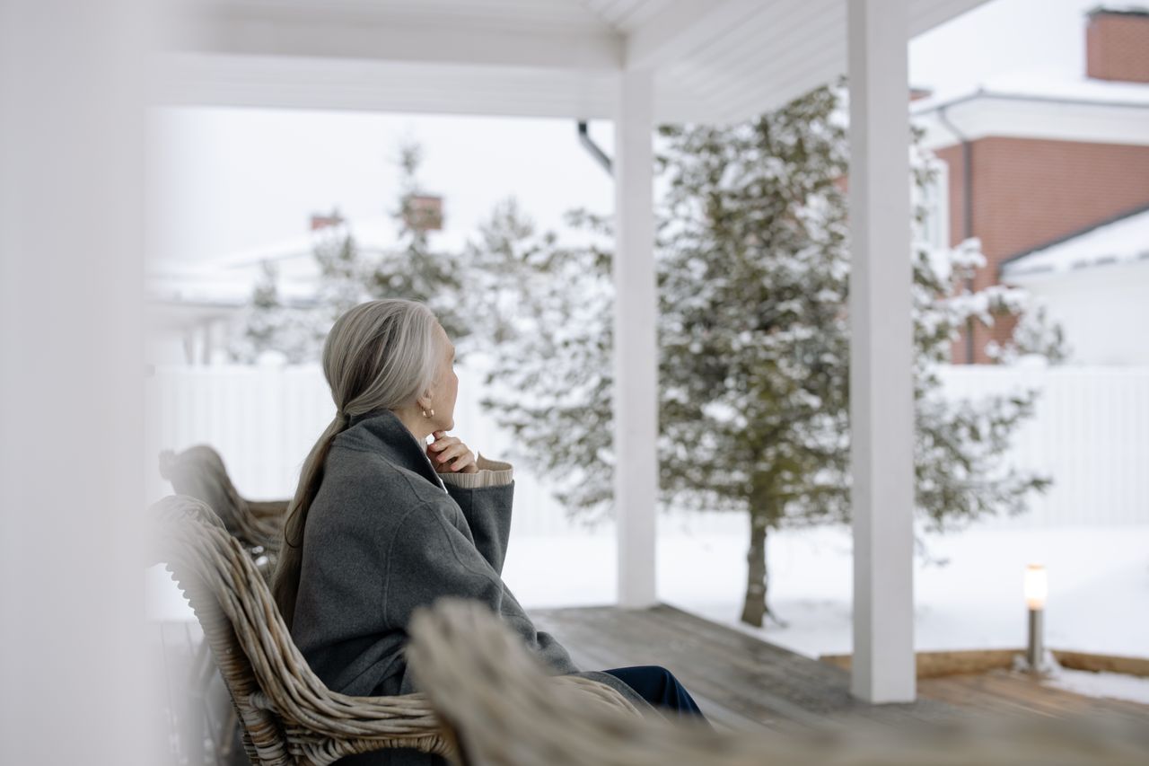 Home Senior woman sitting on porch in winter, enjoying serene snowy view.
