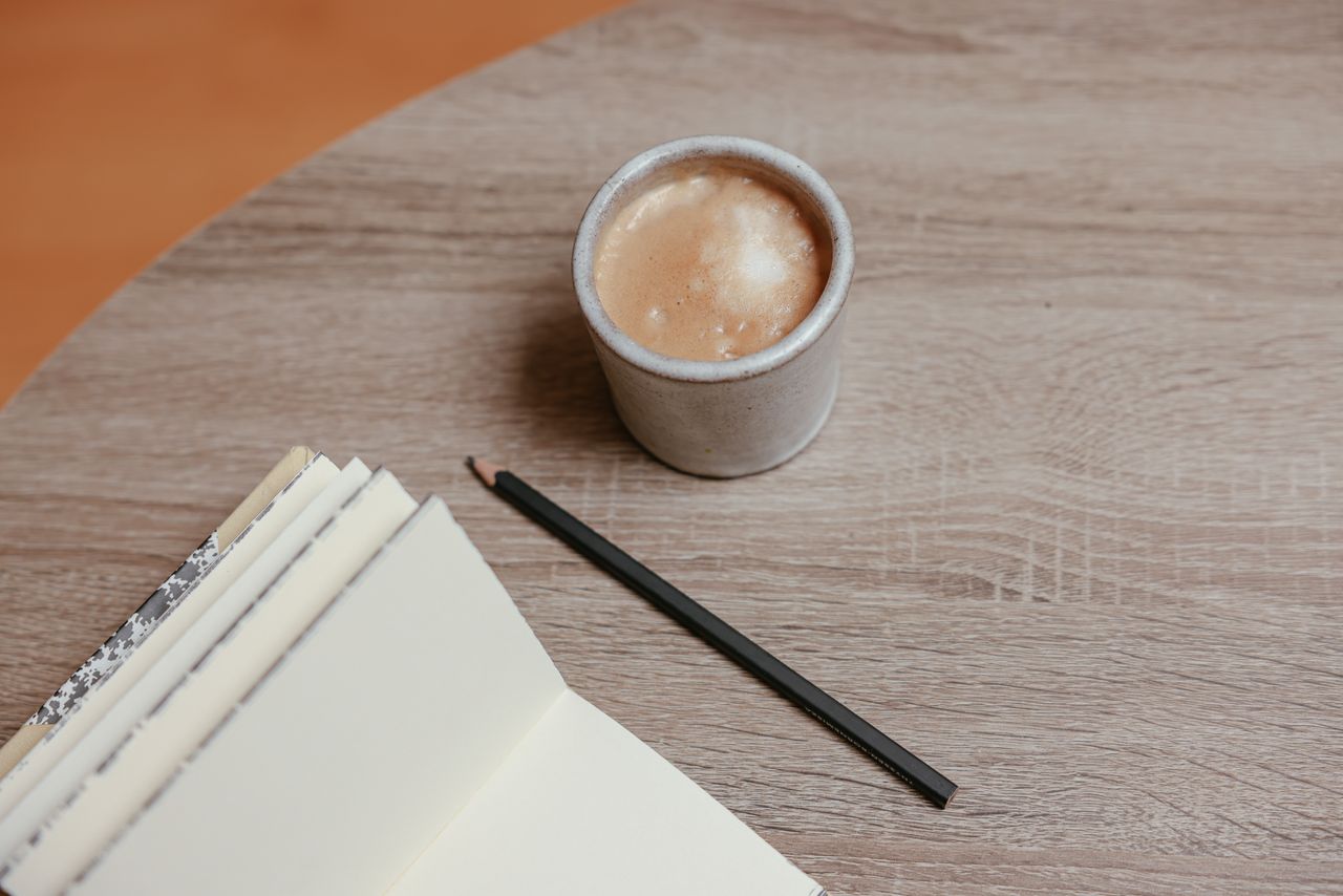 Home A cozy workspace with a coffee cup, open notebook, and pencil on a wooden table.